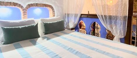A bedroom with a large bed, a window with a view, and a decorative wall.