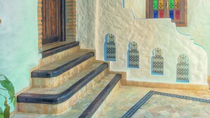 Una escalera con una puerta de madera y un ventanal colorido, que conduce a una habitación con pared blanca y un farol colgante.