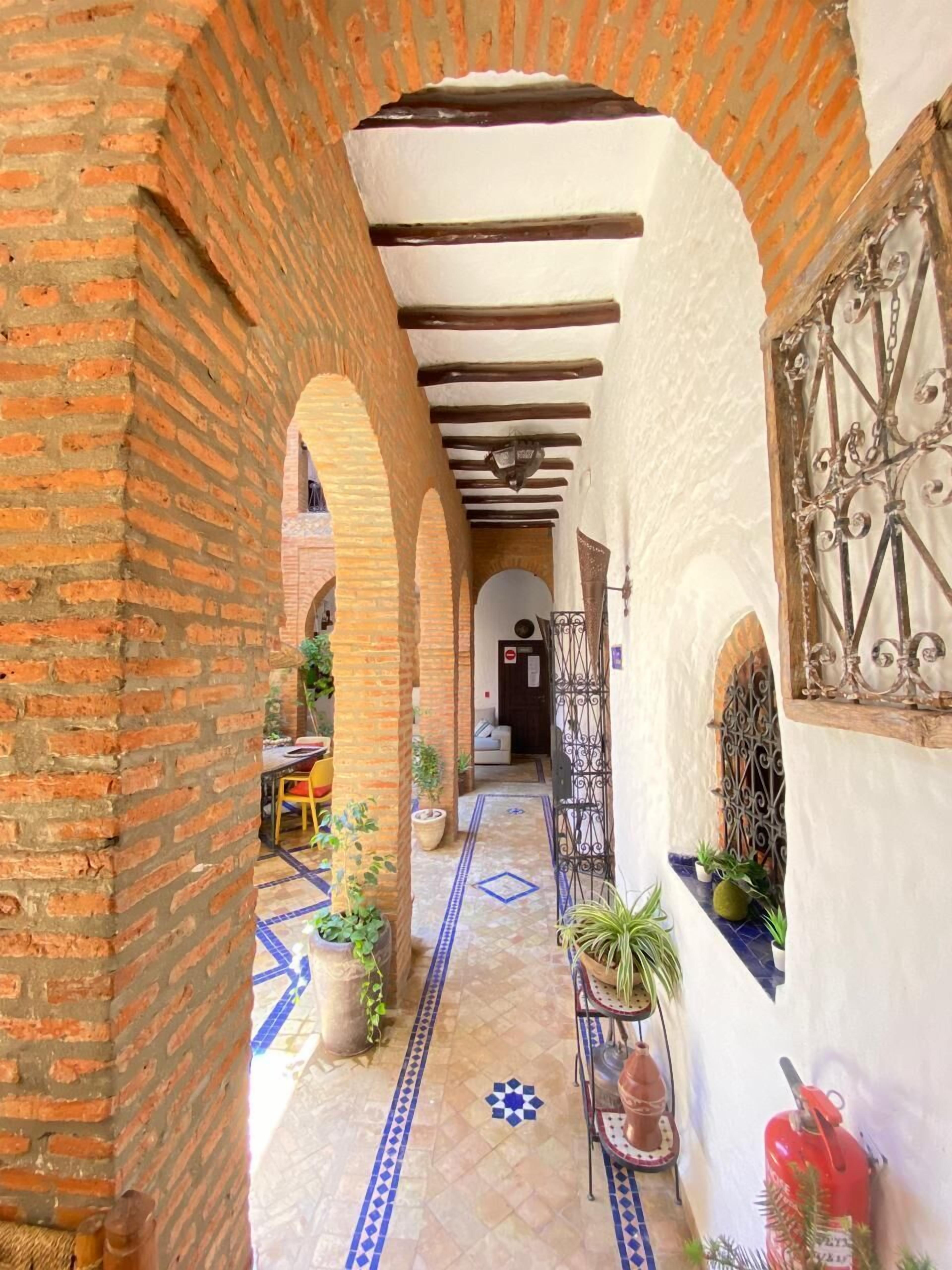 A narrow corridor with brick arches and a tiled floor, leading to a room with a white wall and a metal gate.