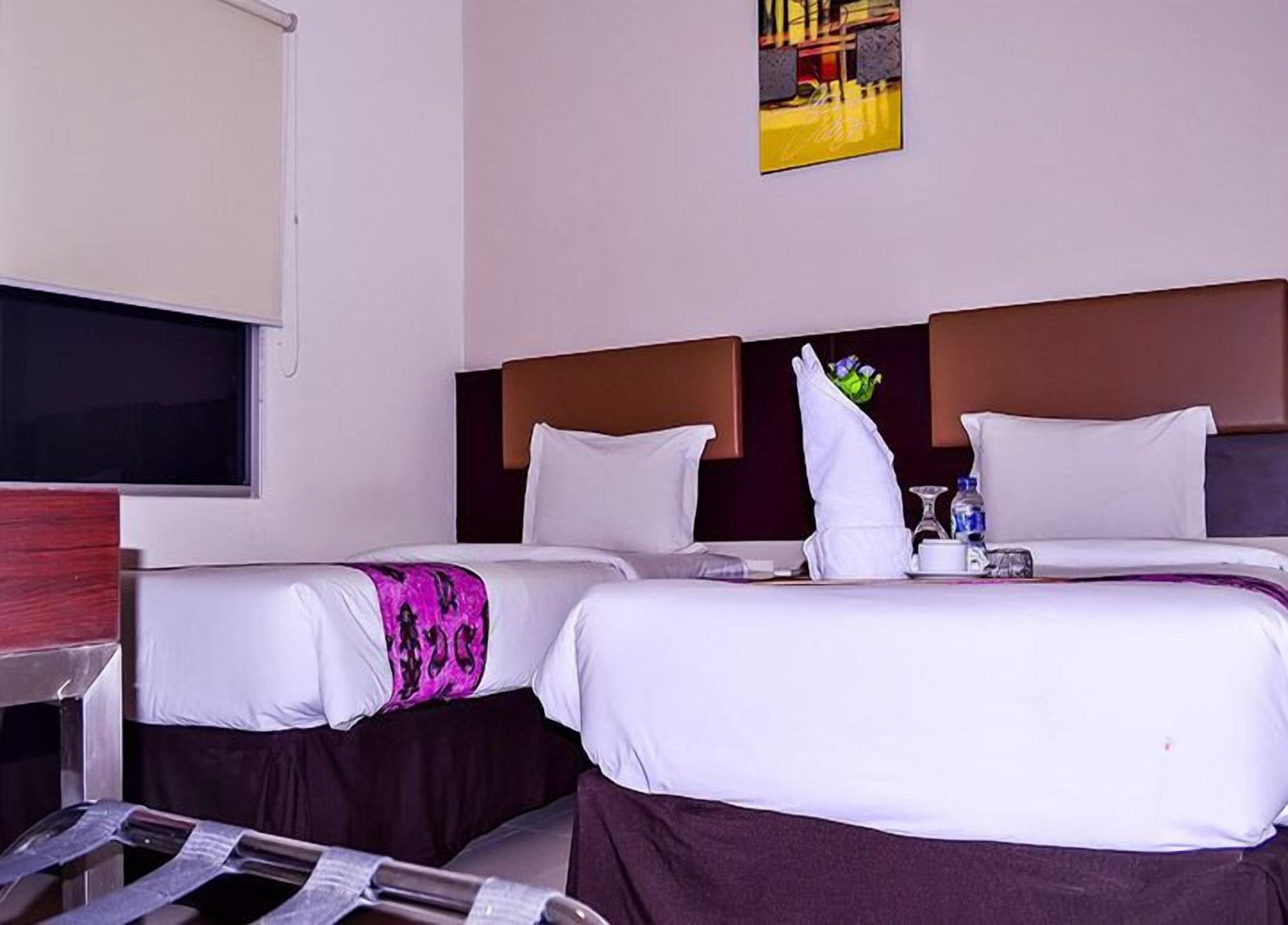 A hotel room with two beds, a flat-screen TV, and a painting on the wall.