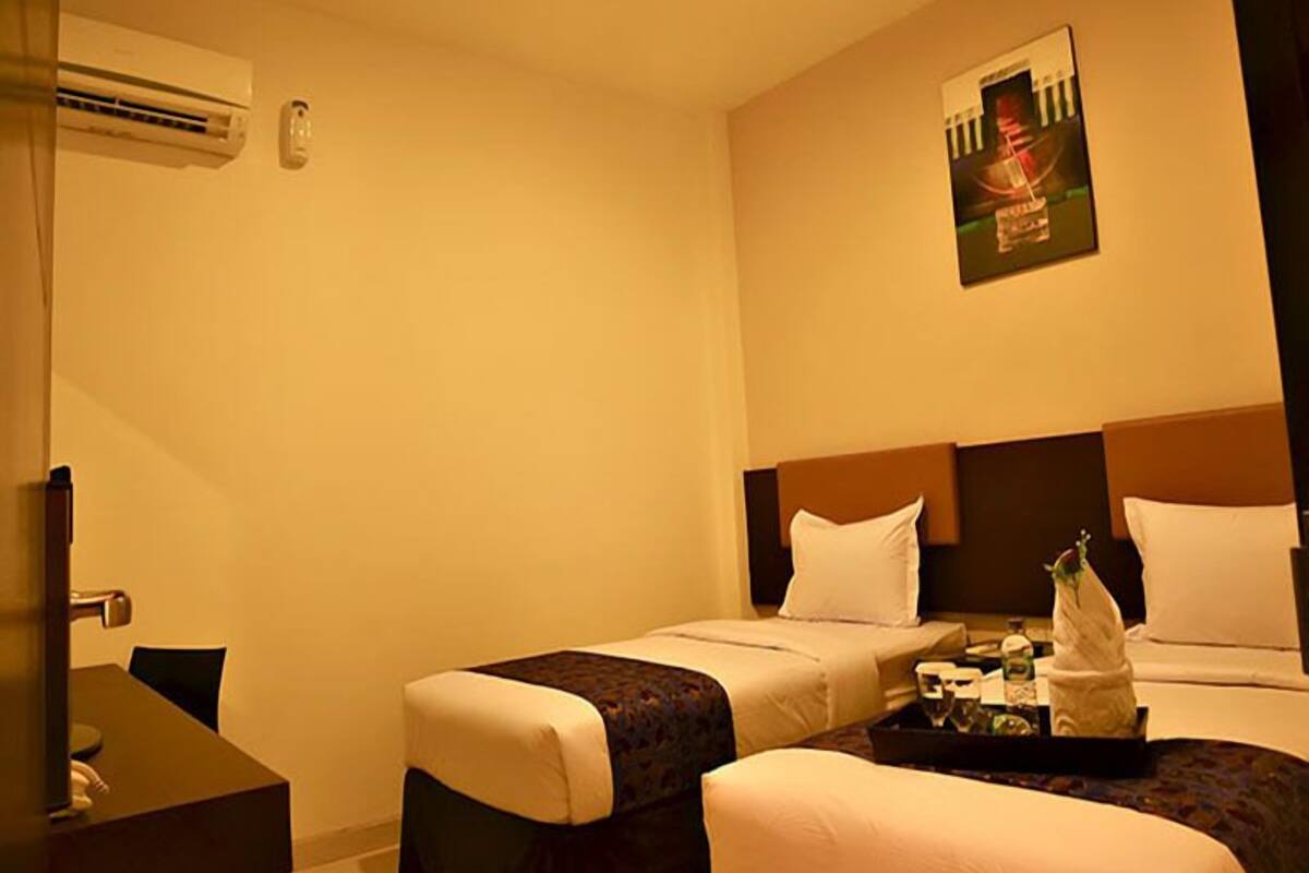 A hotel room with two beds, a desk, and an air conditioning unit.