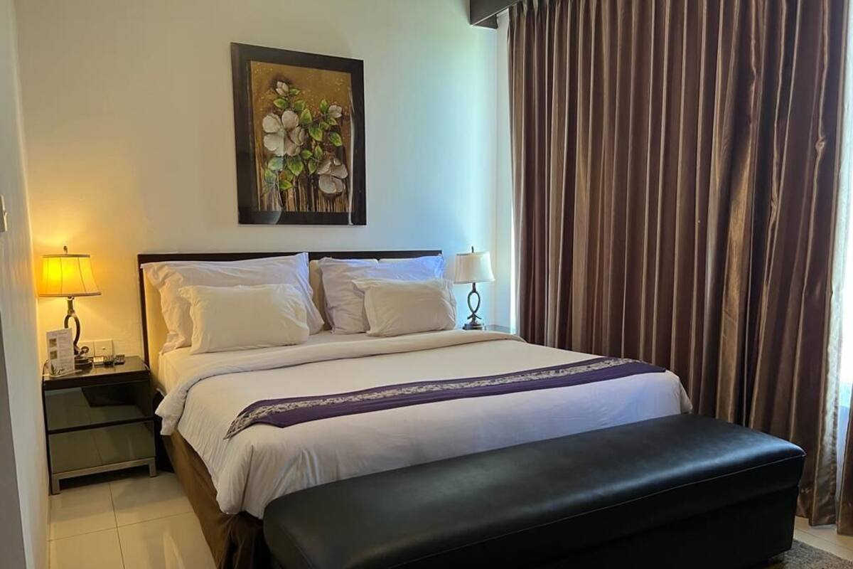 A hotel room with a large bed, a bench, a nightstand, and a painting on the wall.
