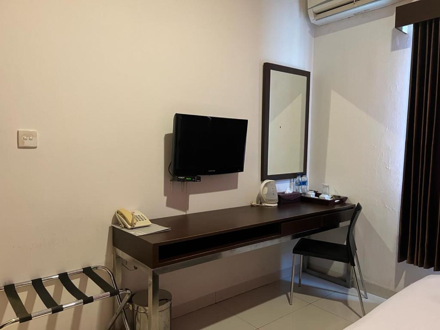 A hotel room with a desk, chair, and a television mounted on the wall.