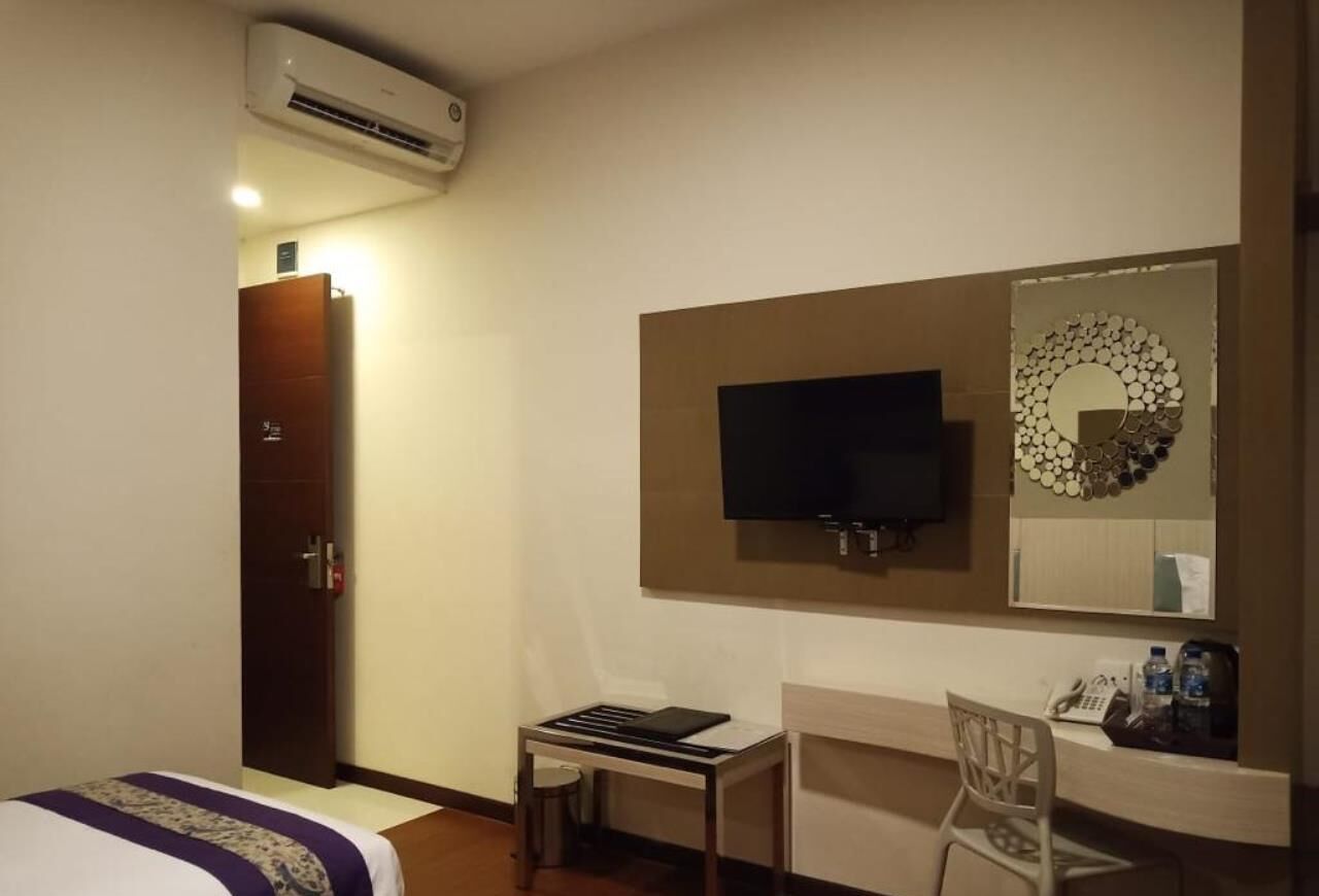 A hotel room with a bed, desk, chair, TV, and a wall-mounted mirror.