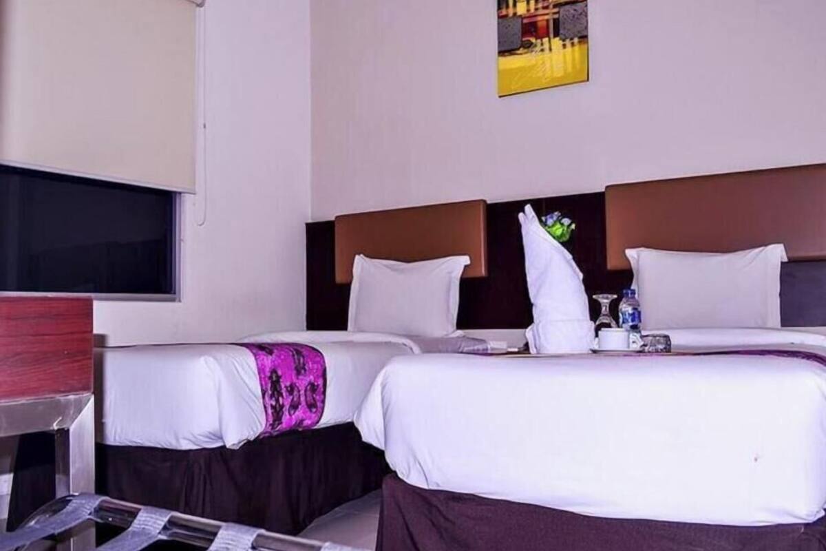 A hotel room with two beds, a flat-screen TV, a painting on the wall, and a window.