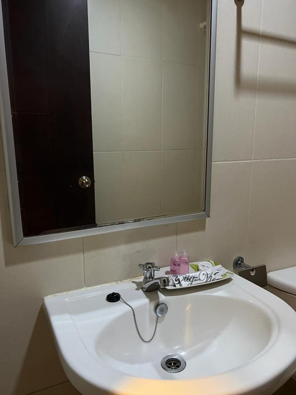 Un baño con un lavamanos blanco, un espejo encima y un inodoro a la derecha.