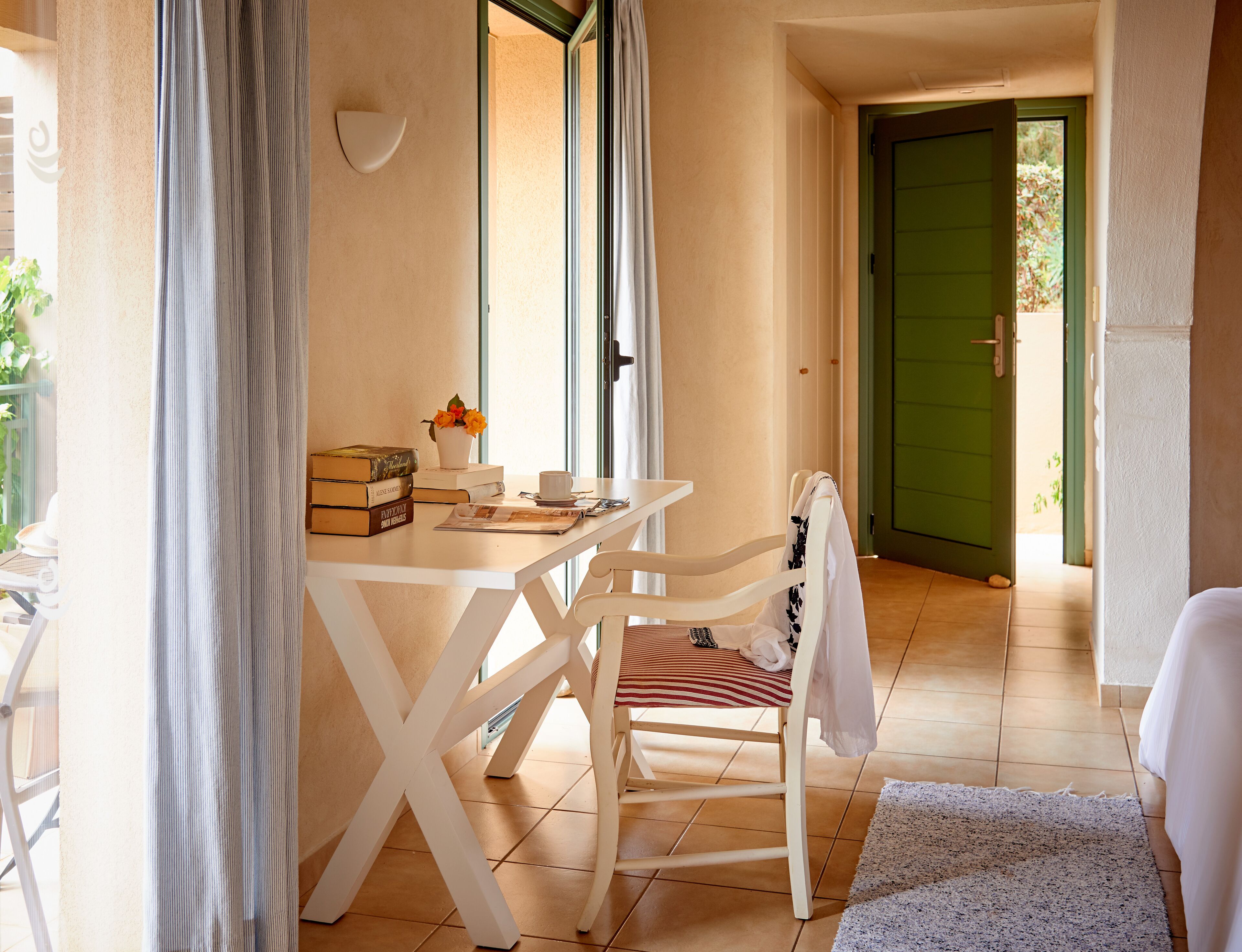 Ein Zimmer mit einem weißen Tisch, einem Stuhl, einer kleinen weißen Vase mit Blumen und einer grünen Tür im Hintergrund.
