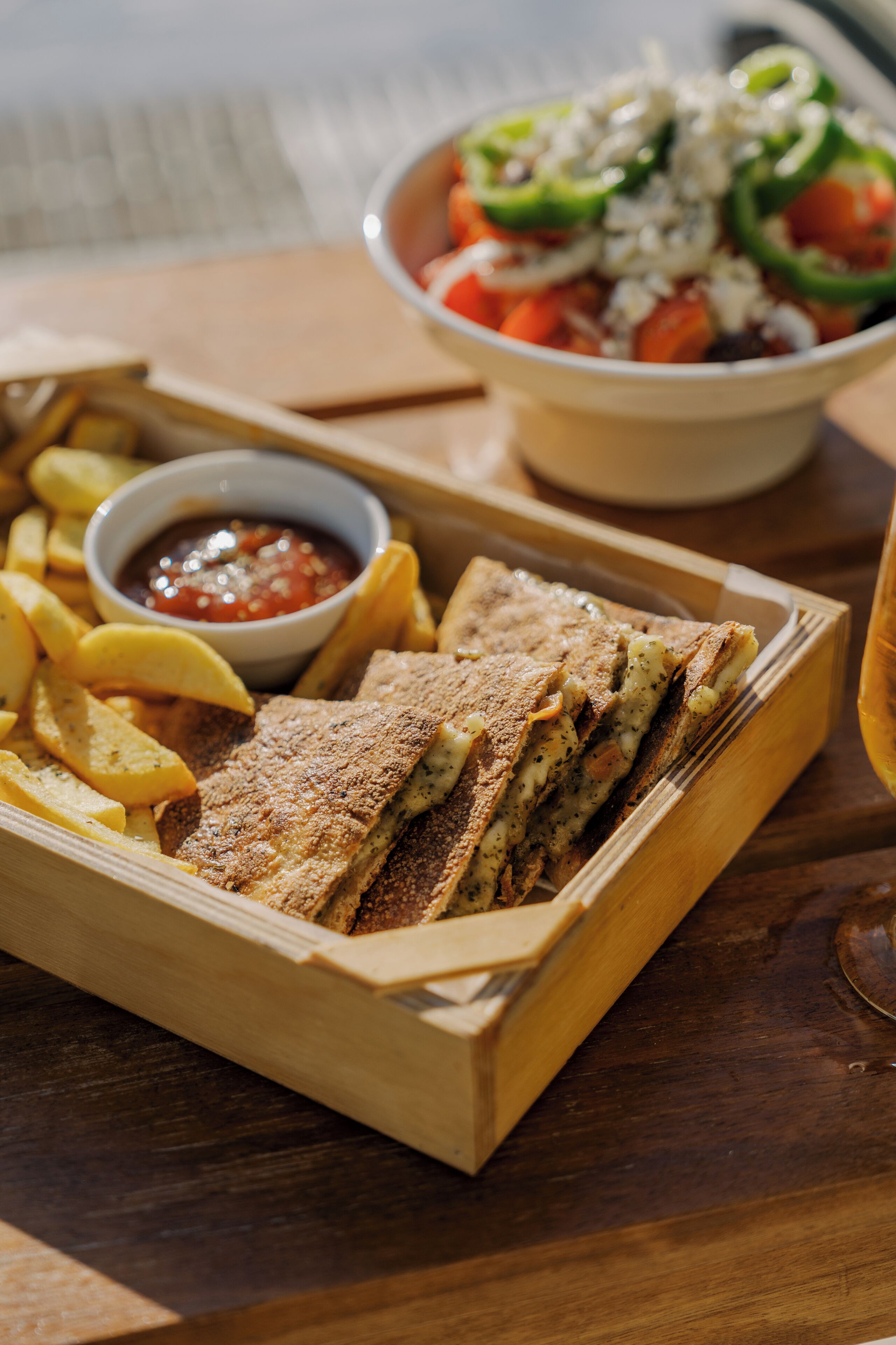 A wooden tray with a sandwich, fries, and a bowl of salad.