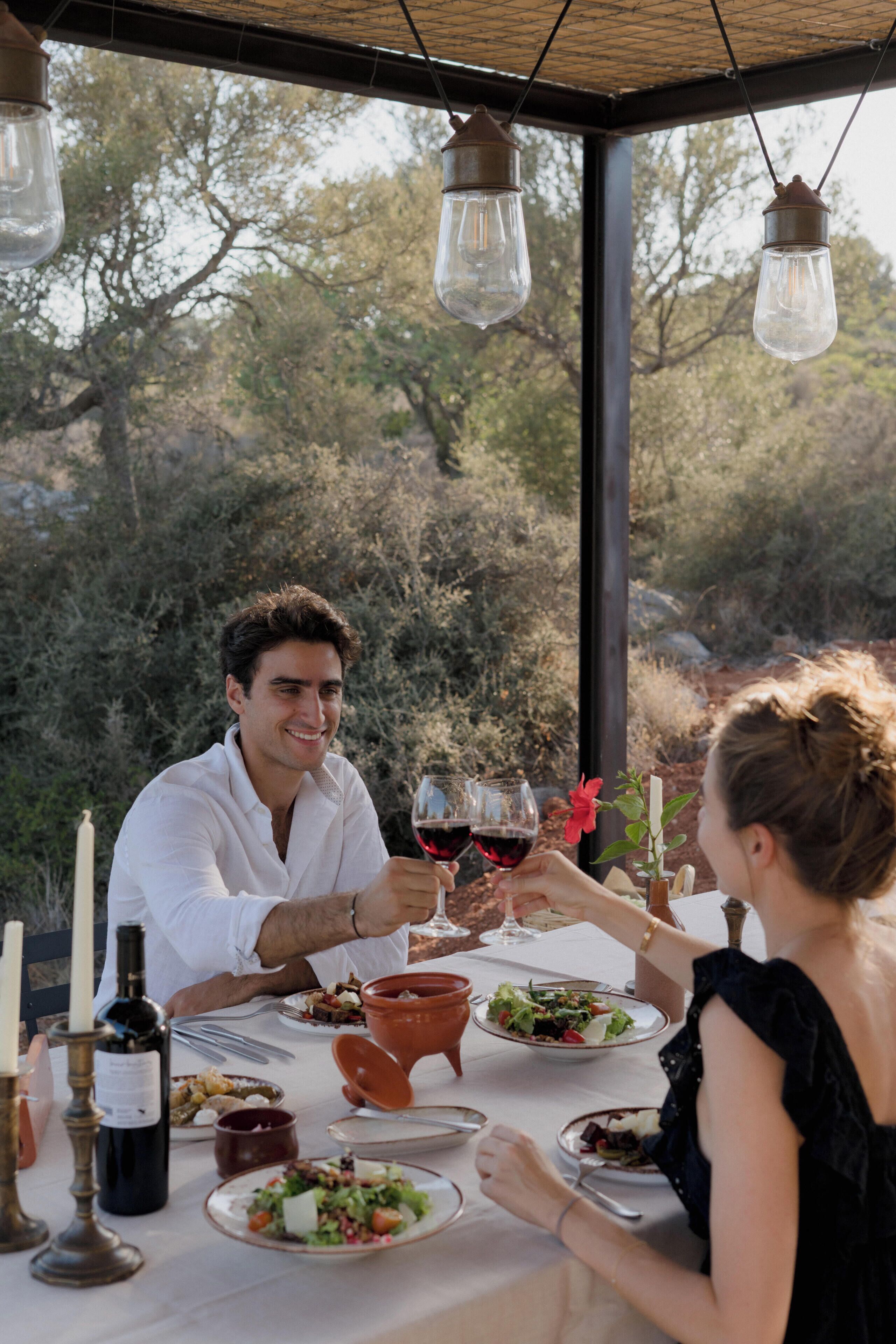 Una mesa de comedor lista para dos personas, con copas de vino, una botella de vino y platos de comida.