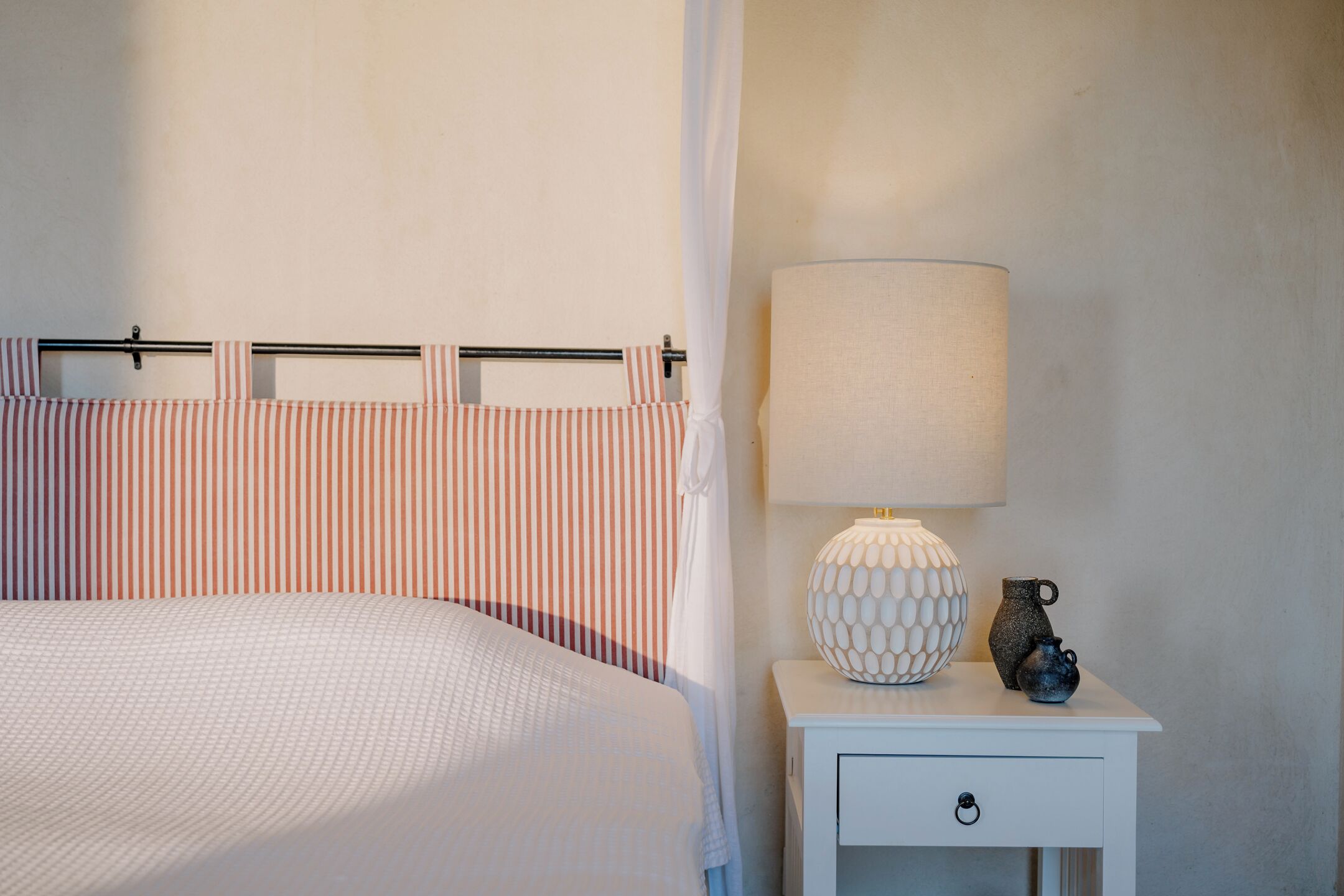 A neatly made bed with a striped headboard, a bedside lamp, and a small table with decorative items.