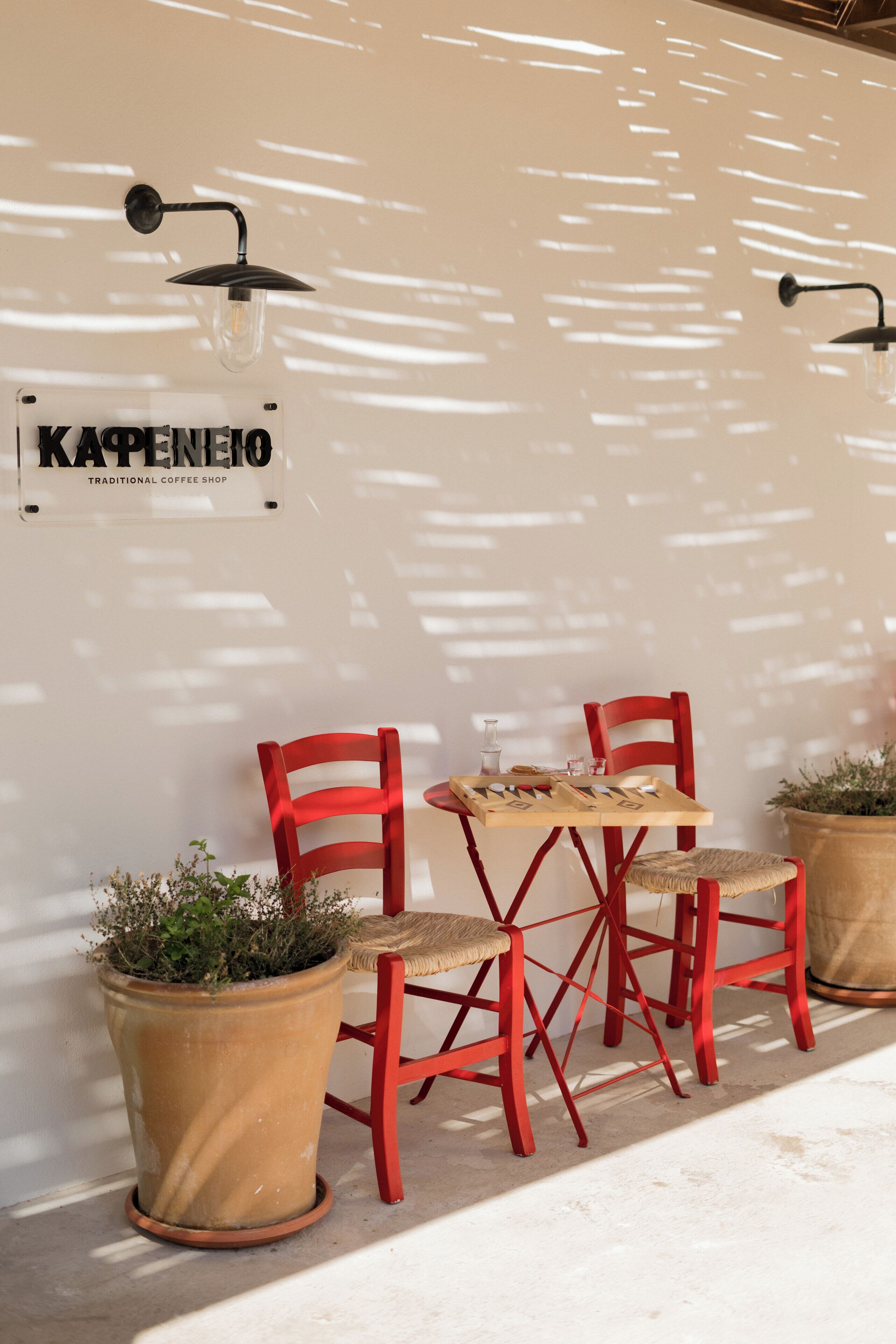 A traditional coffee shop with two red chairs, a small table, and potted plants.