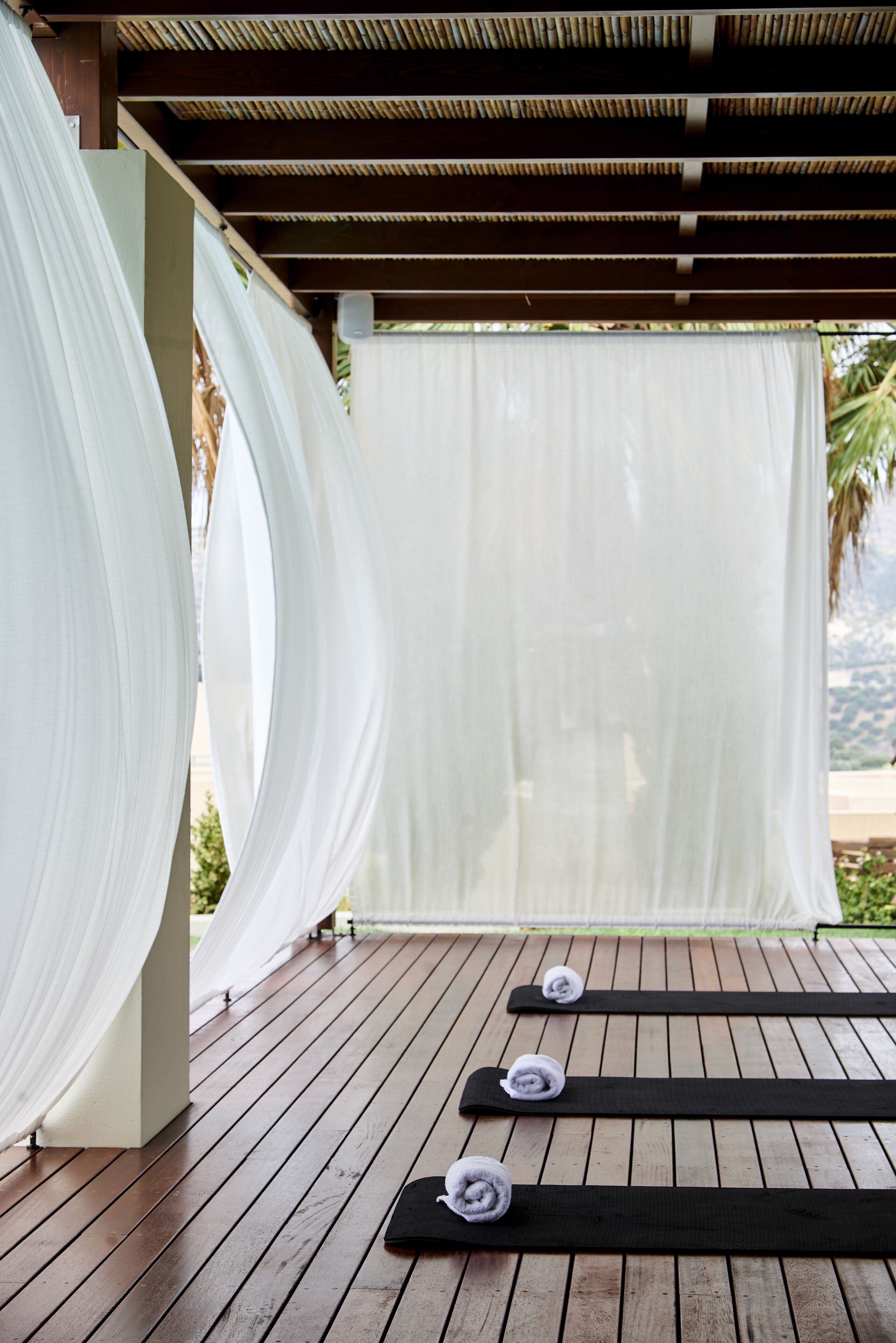 A wooden deck with white curtains and black mats.
