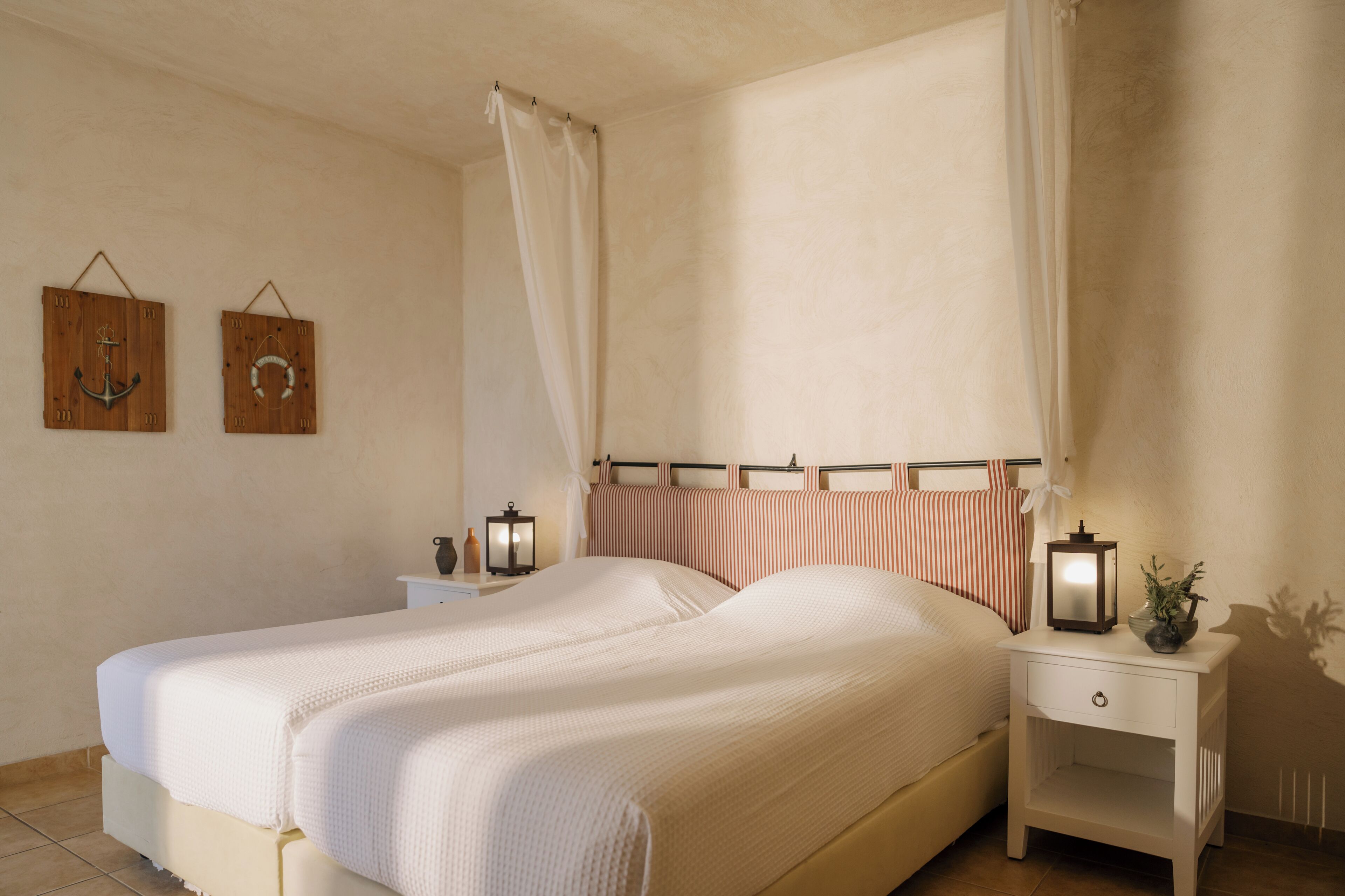 A double bed with a canopy, two bedside tables with lamps, and a small nightstand with a plant.