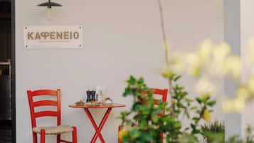 Una cafetería tradicional con un letrero que dice "Капенео". Hay dos sillas rojas y una mesa pequeña con una cafetera, azúcar y una taza.