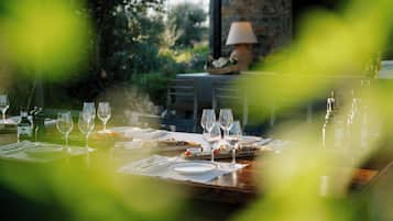 A dining table set with wine glasses, plates, and cutlery, with a lamp and a stone wall in the background.