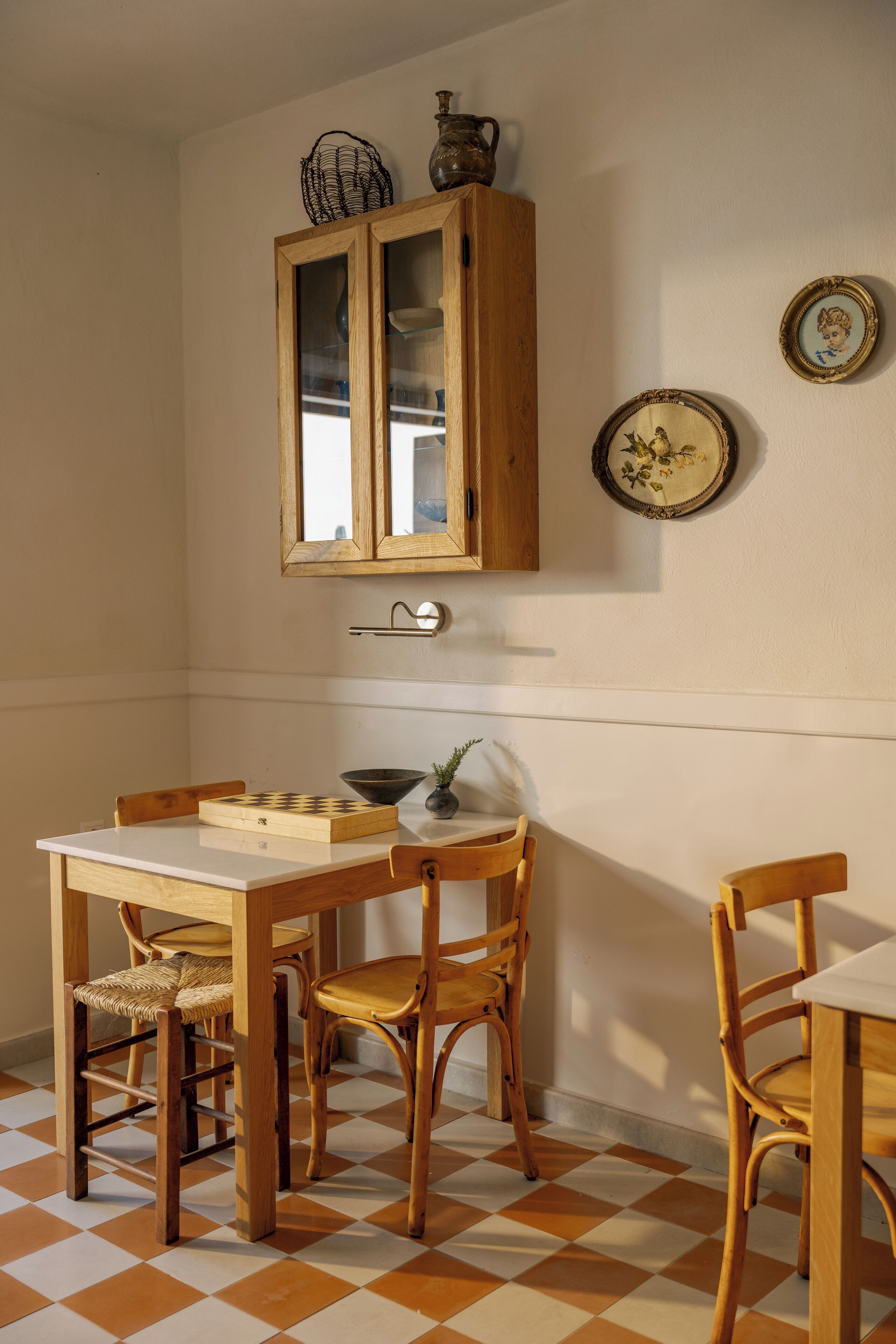 A dining area with a wooden table and chairs, a checkered floor, a cabinet with glass doors, and wall-mounted plates.