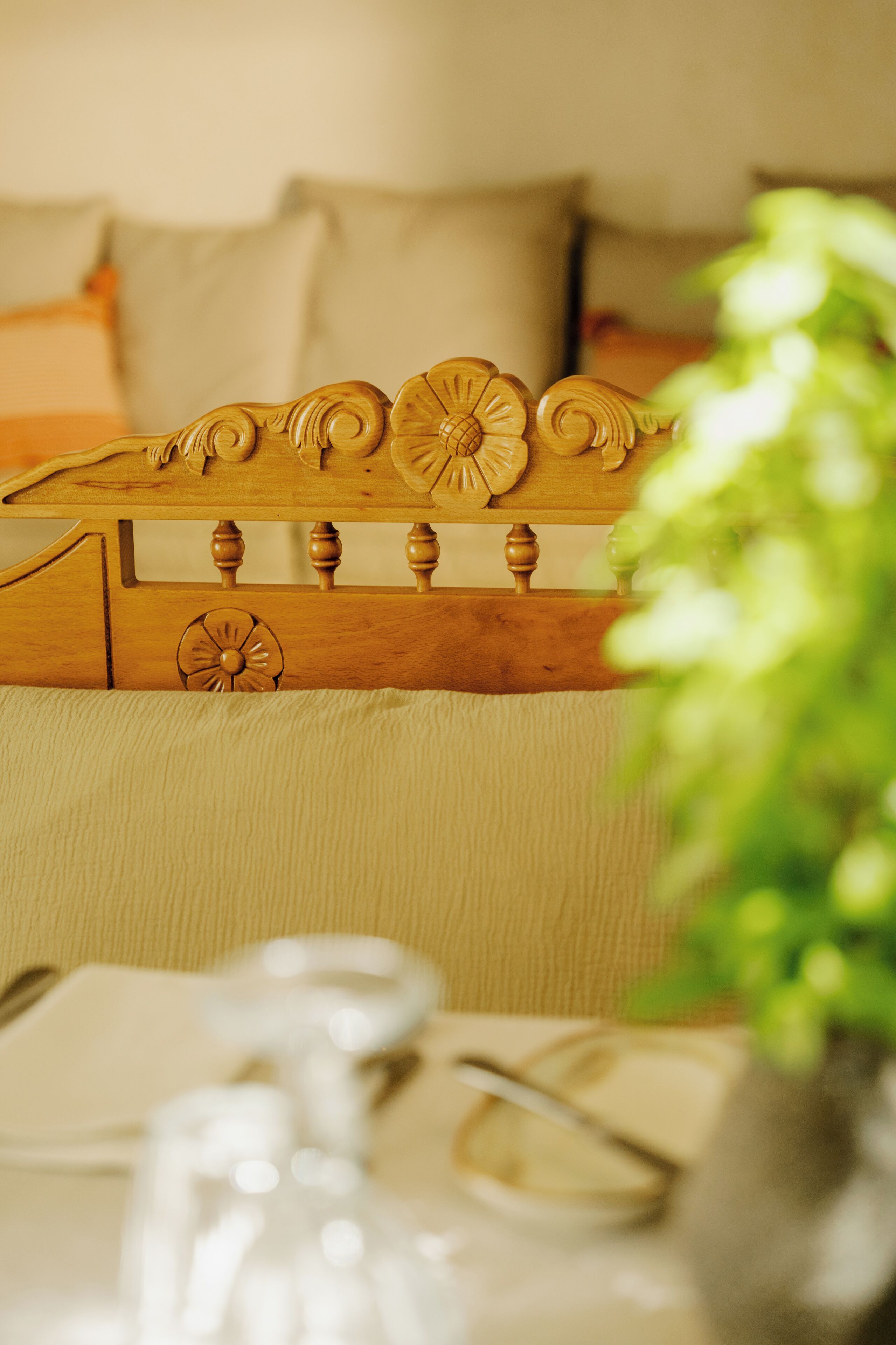 A wooden headboard with intricate carvings, a beige upholstered headboard, and a bedside table with a glass vase and a book.