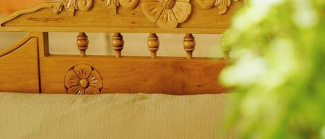 A wooden headboard with intricate carvings, a beige upholstered headboard, and a bedside table with a glass vase and a book.