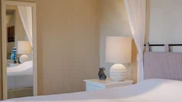 A neatly made bed with a white comforter, a bedside table with a lamp and a vase, and a mirror on the wall.
