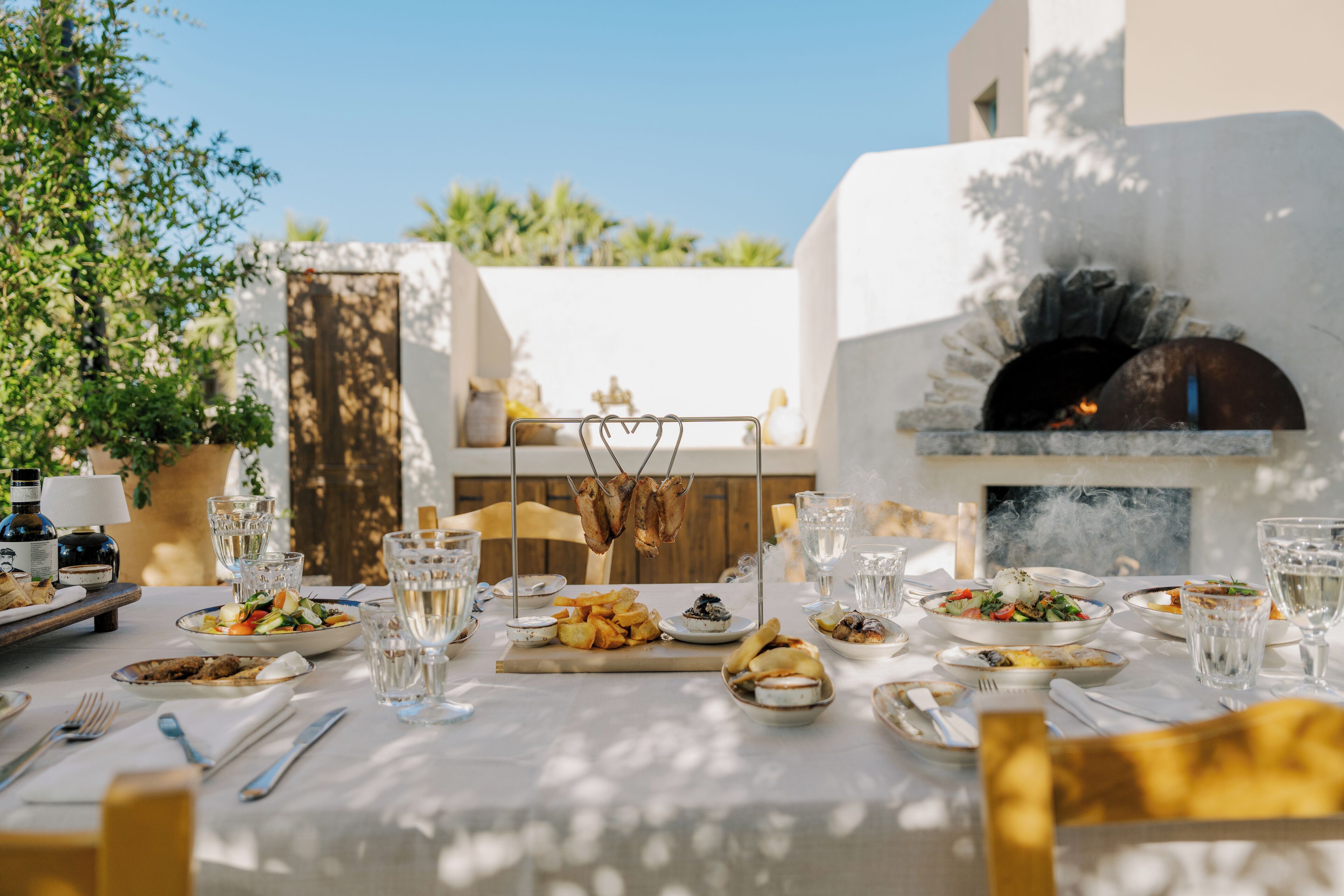 An outdoor dining area with a stone oven, various dishes, and glasses on a table.