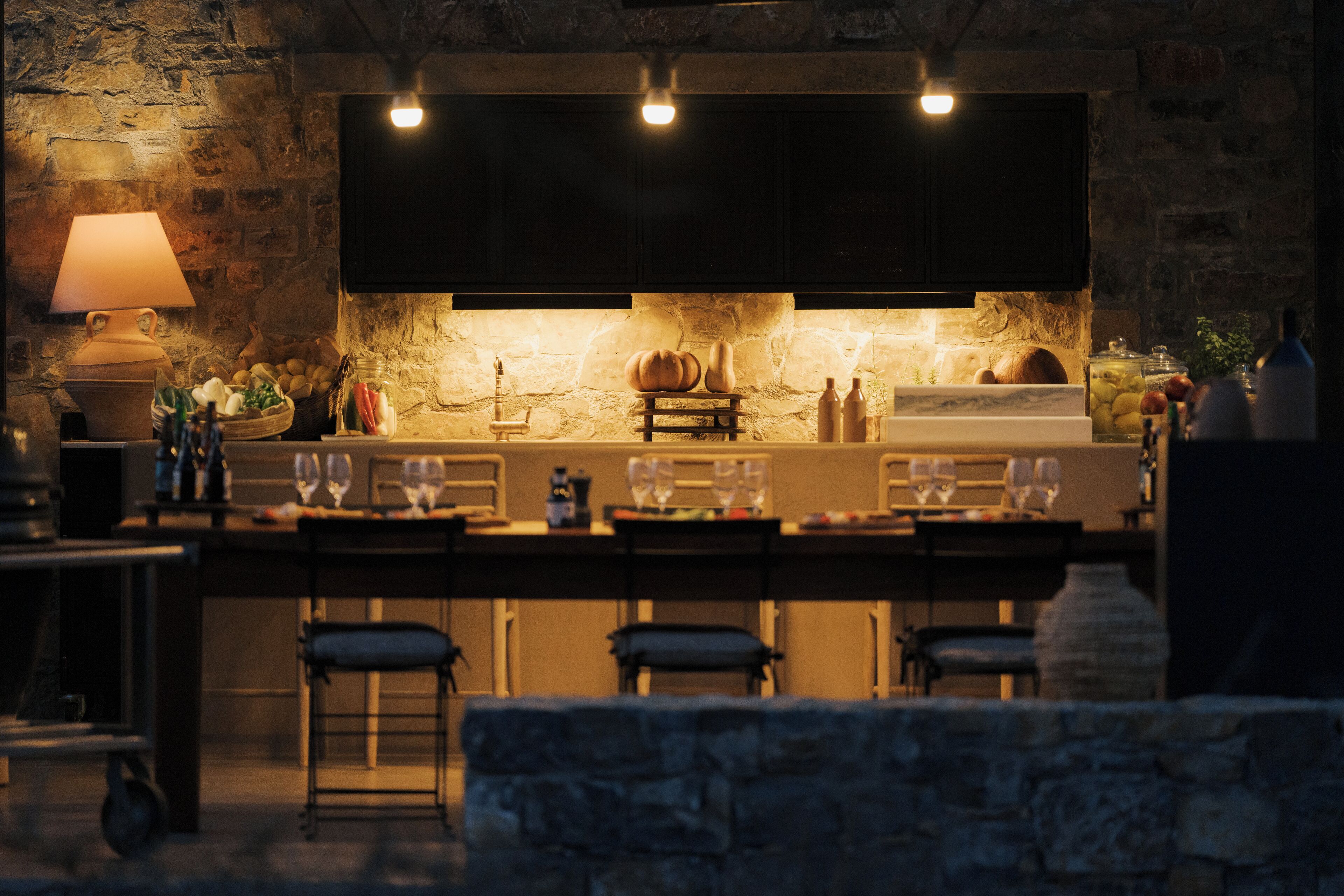 A rustic kitchen with a stone wall, wooden bar, and a hanging light fixture.