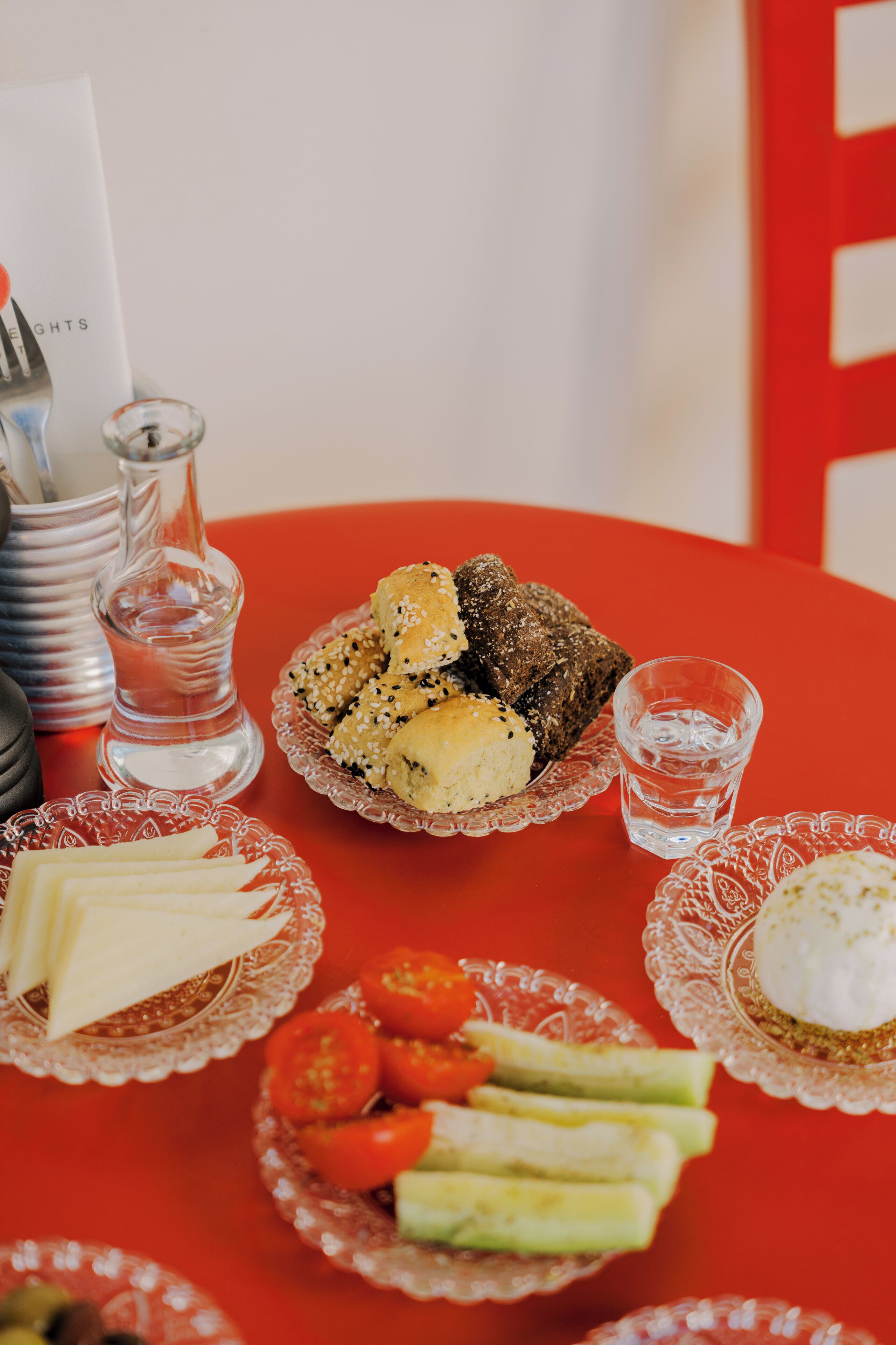 A table with various food items, including bread, cheese, and vegetables, on a red tablecloth.