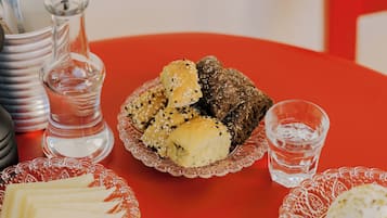 A table with various food items, including bread, cheese, and vegetables, on a red tablecloth.
