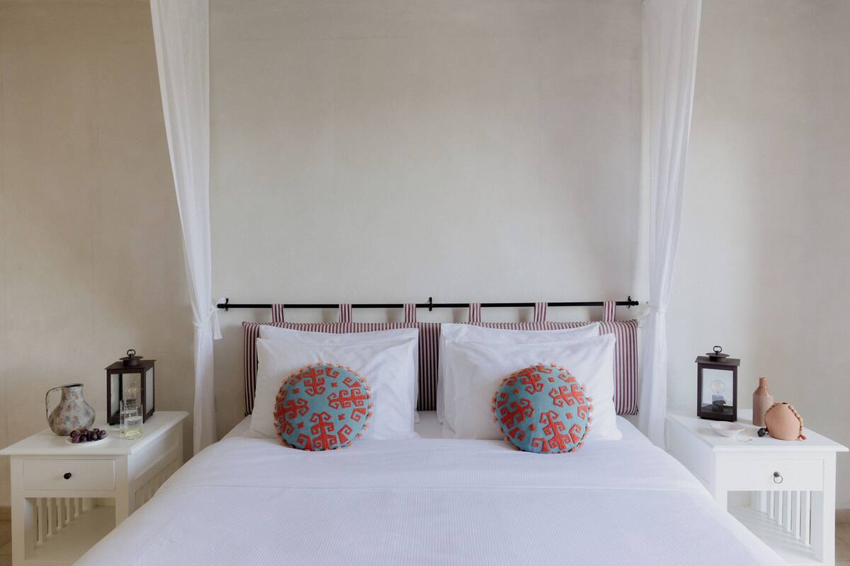 A neatly arranged bedroom with a canopy bed, two bedside tables, and a nightstand.