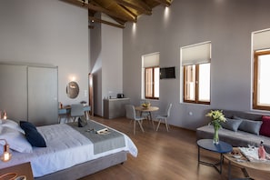 A modern bedroom with a bed, bedside table, and a desk area with a chair and a small table. - Bluebell Luxury Suites (Chania)