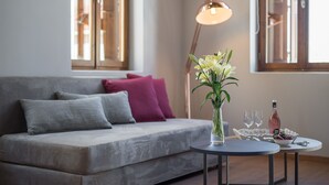 Una sala de estar moderna con un sofá gris, una mesa redonda con un florero y una botella de vino.