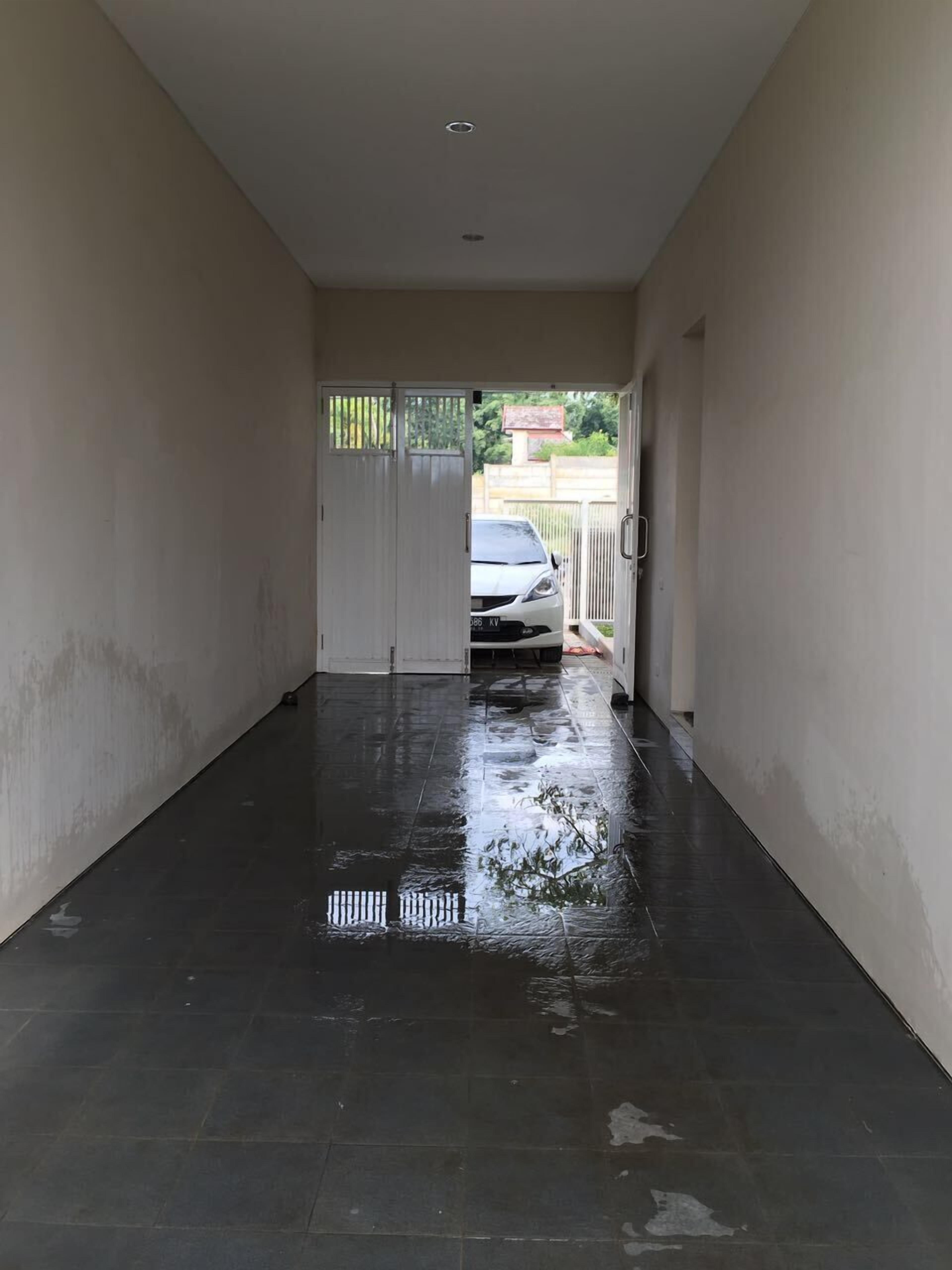 A hallway with a wet floor, leading to a gated area with a parked car visible through the gate.