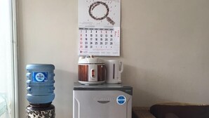 A compact kitchenette with a refrigerator, a coffee maker, and a water dispenser. A calendar is mounted on the wall above the refrigerator. - The Villaku Batu (Batu)