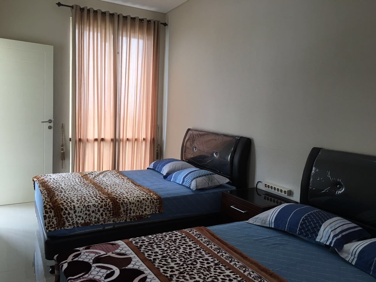 Un dormitorio con dos camas, una ventana con cortinas, una mesita de noche y un enchufe.