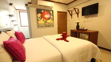 A hotel room with a bed, pillows, a painting, a TV, and a desk with a vase and a cup.