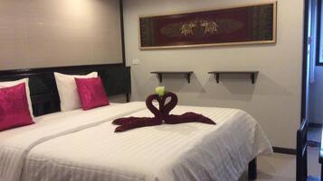A hotel room with two beds, each with white bedding and pink pillows. There is a decorative swan towel on the bed in the foreground. The room has a modern design with a dark headboard and a wall-mounted air conditioner.