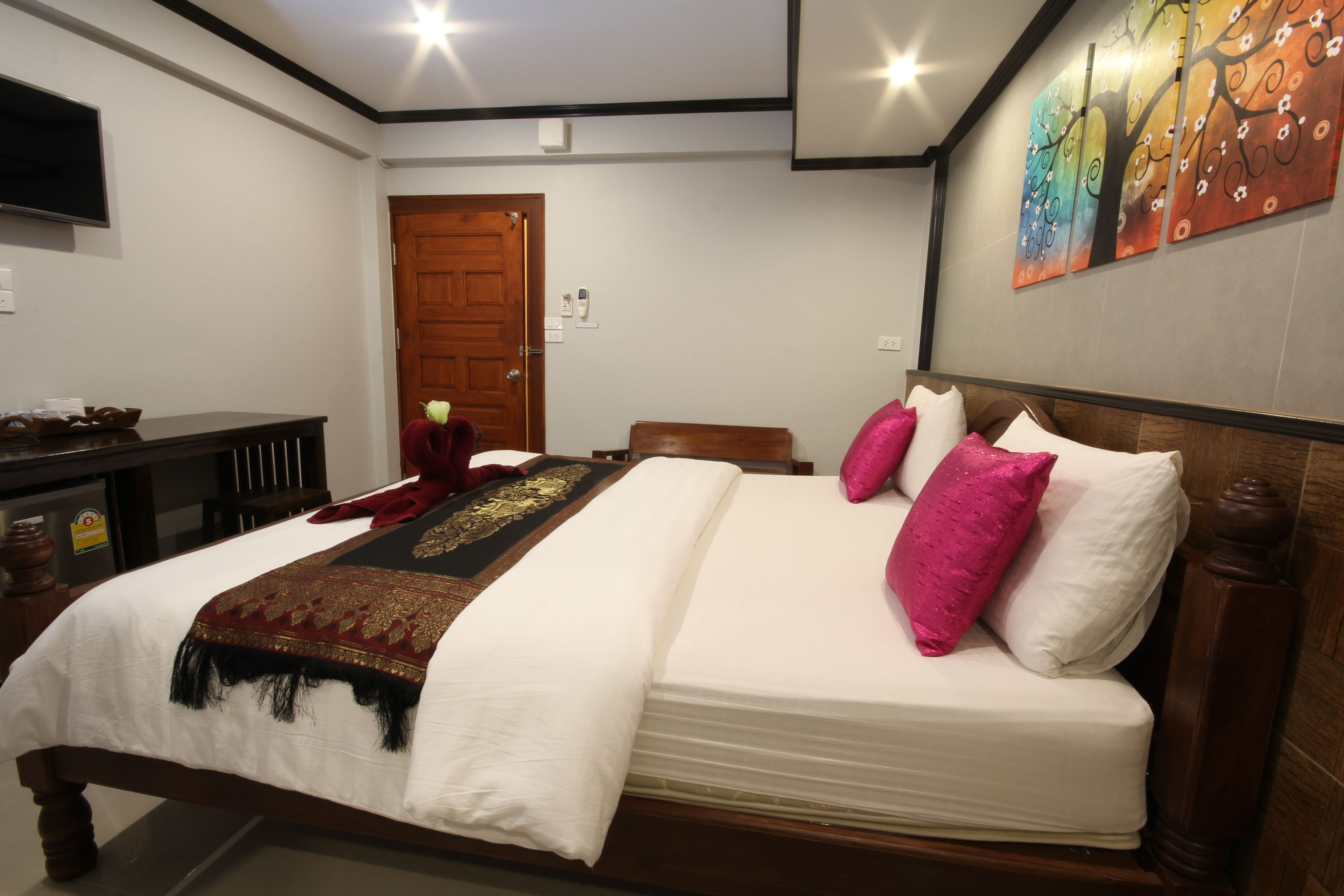 Una cama bien hecha con una colcha blanca y roja, dos almohadas rosas y un cabecero de madera.