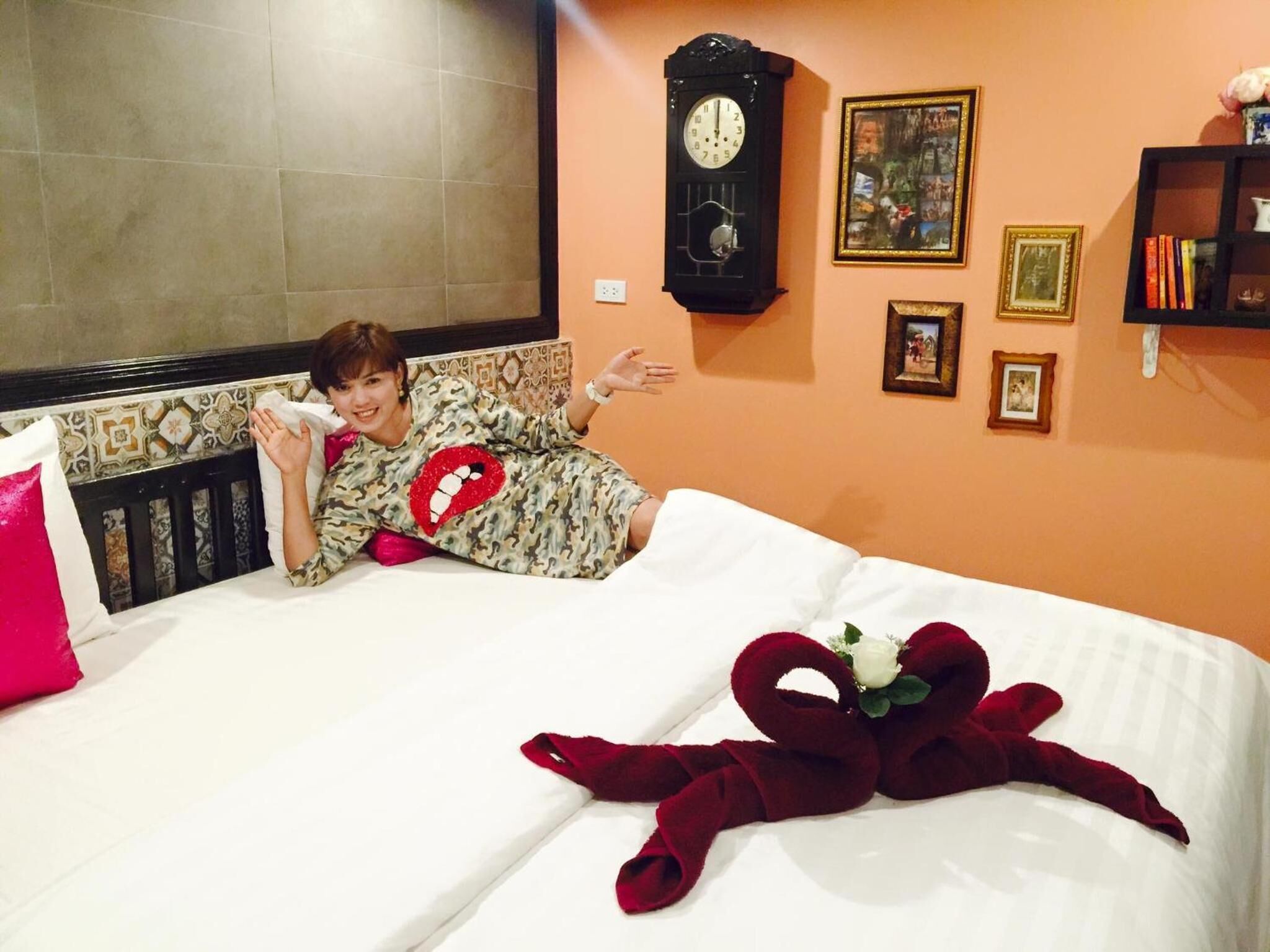A bed with a red heart-shaped pillow, a clock, and framed pictures on the wall.
