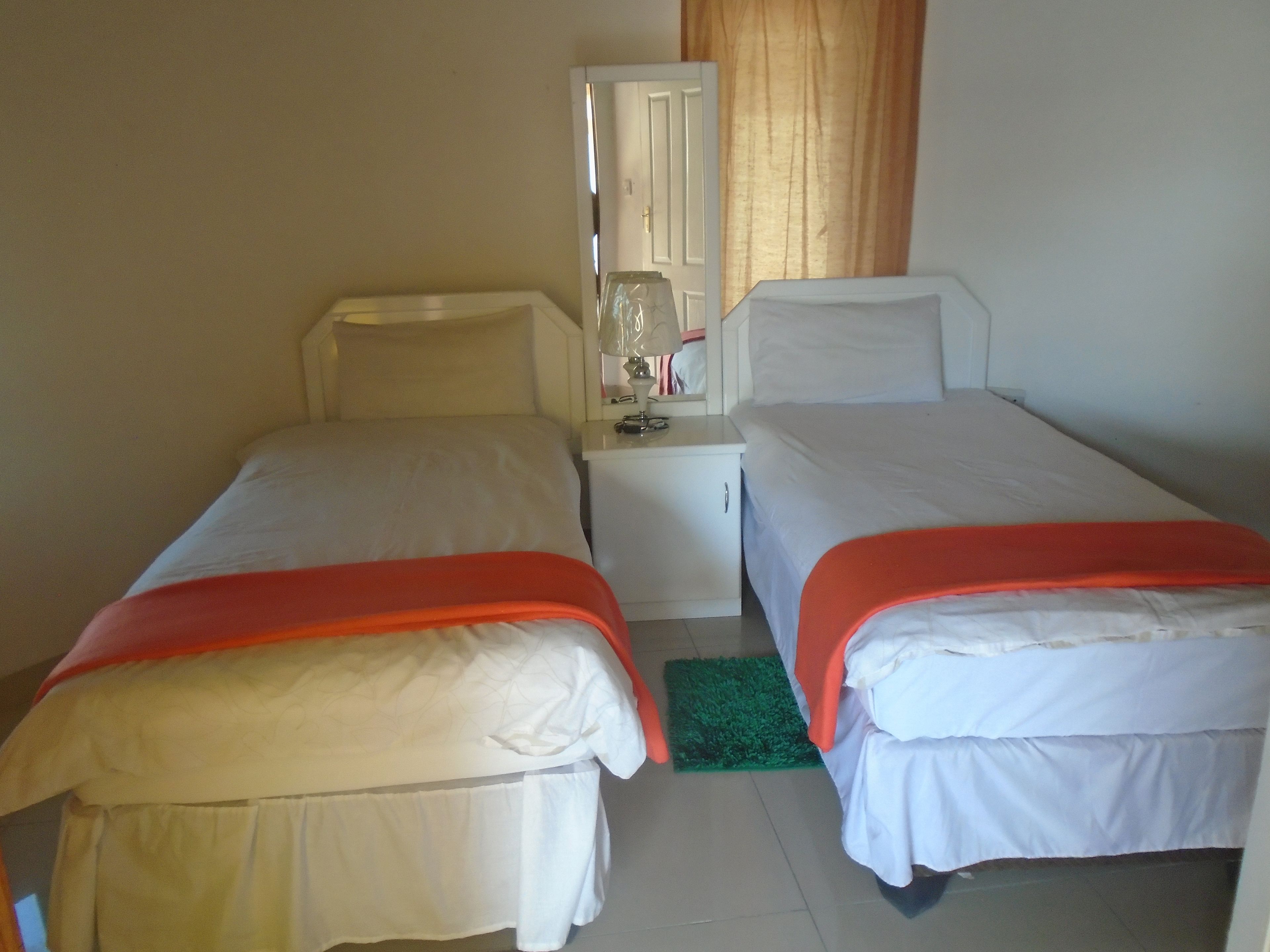 A twin room with two beds, a nightstand, a mirror, and a green rug.