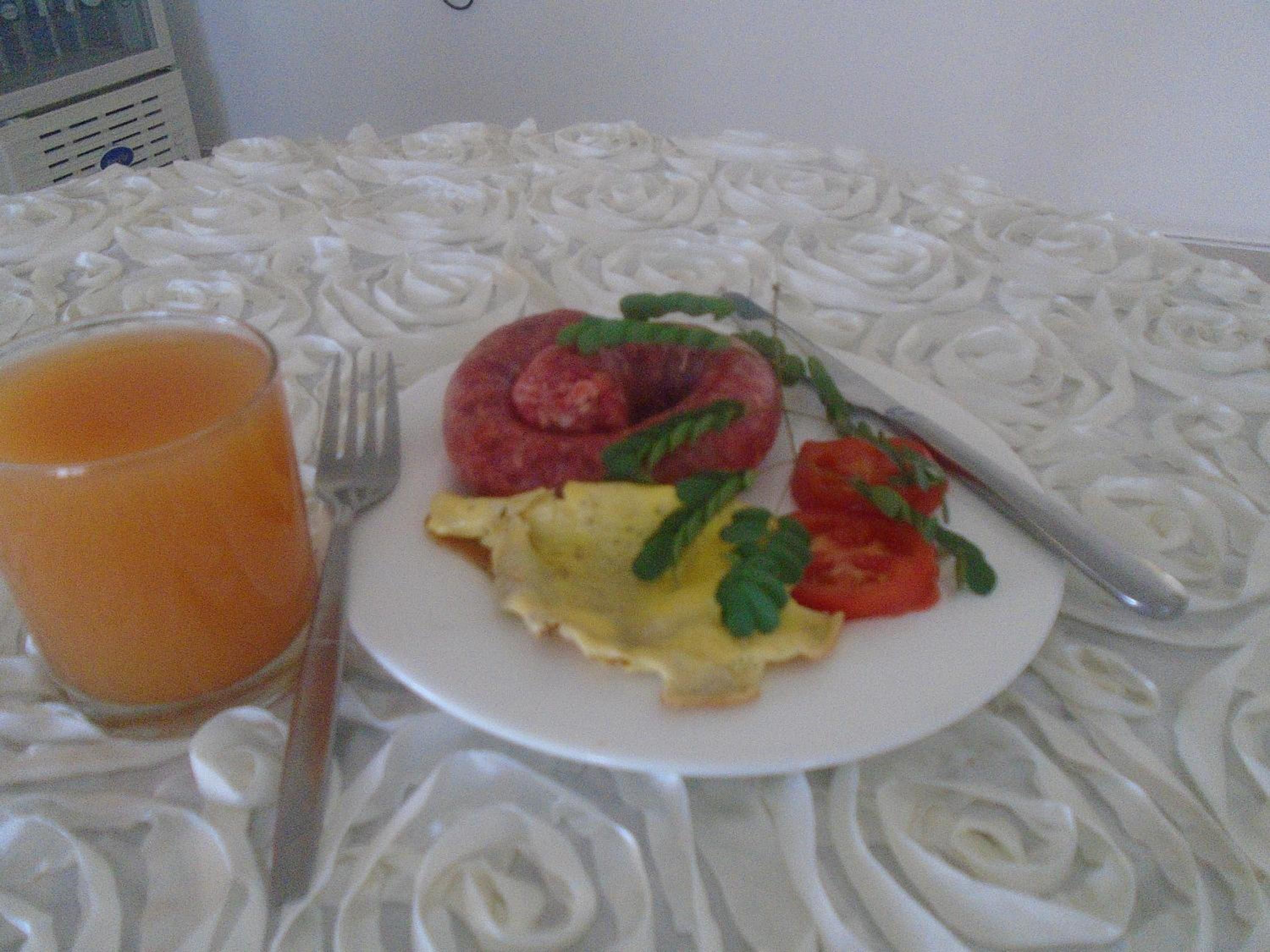Un plato con huevos revueltos, una rodaja de tomate y un elemento rojo, posiblemente una fruta o verdura, sobre un mantel blanco.