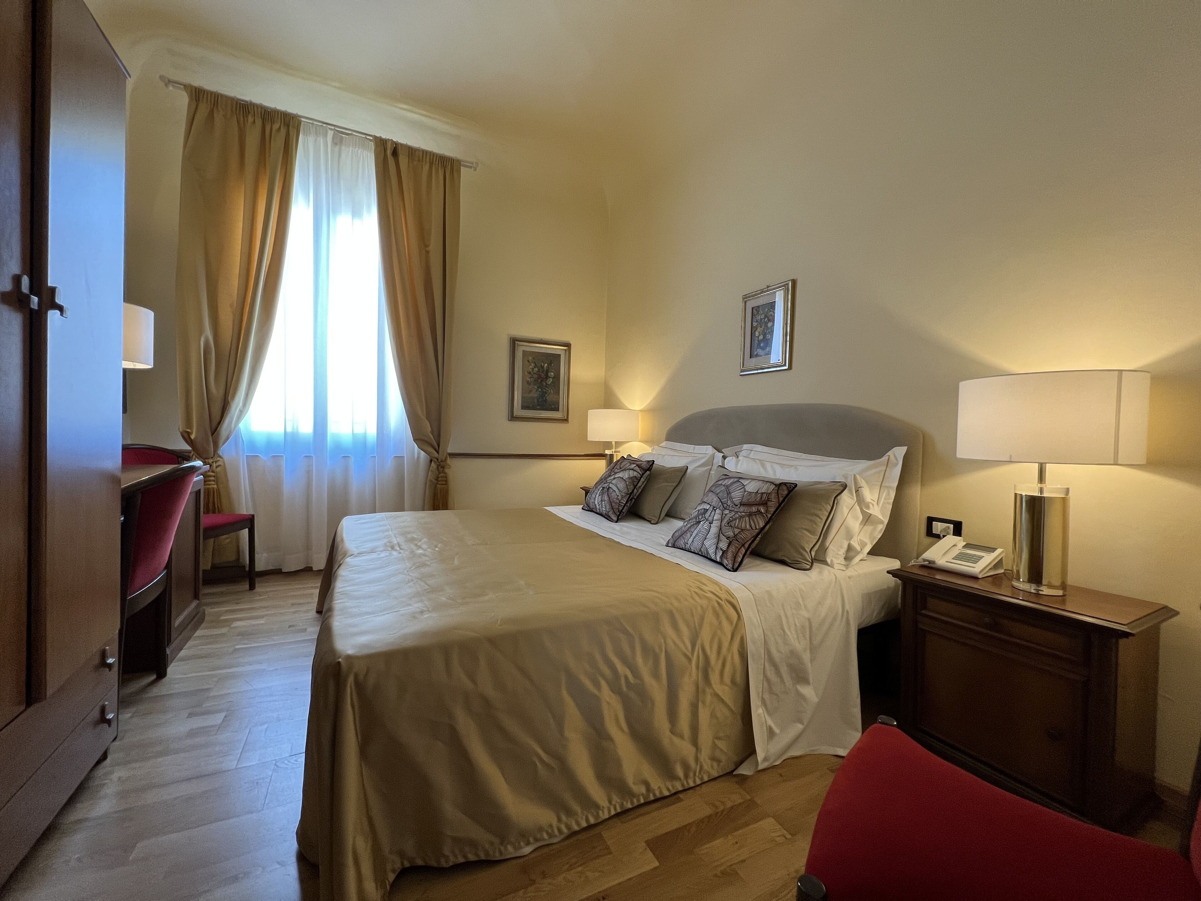 A hotel room with a large bed, a desk, a chair, a bedside table with a lamp, and a telephone.