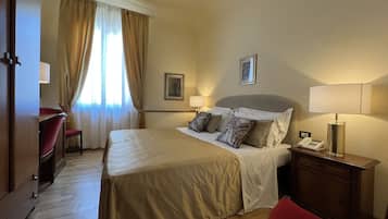 Una habitación de hotel con una cama grande, un escritorio, una silla, una mesita de noche con lámpara y un teléfono.