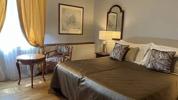 A hotel room with a large bed, a chair, a small table, a lamp, and a framed map on the wall.