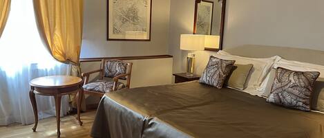 Ein Hotelzimmer mit einem großen Bett, einem Sessel, einem kleinen Tisch, einer Lampe und einer gerahmten Karte an der Wand.