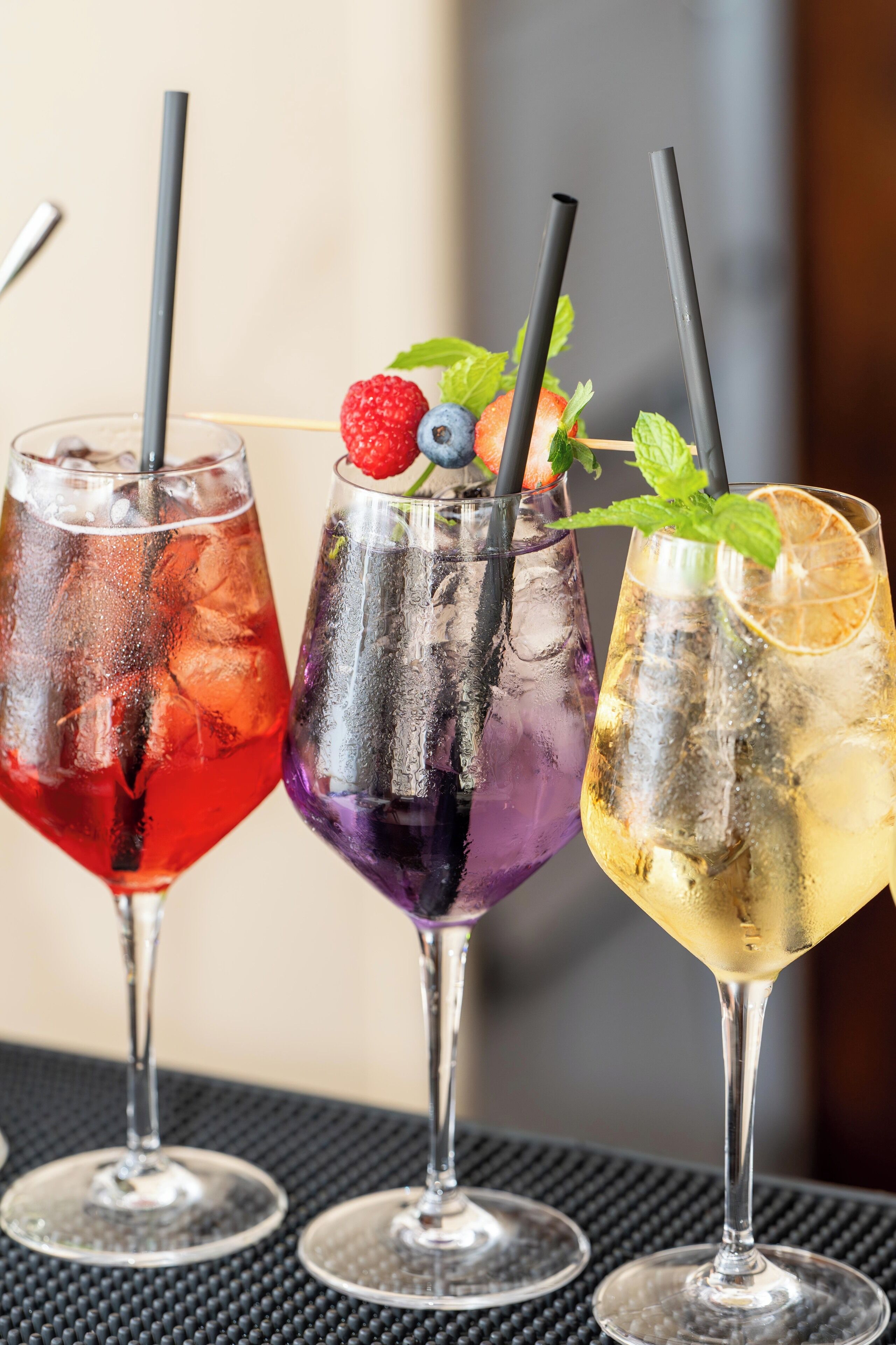 Three glasses of cocktails with straws, garnished with fruits and mint leaves.