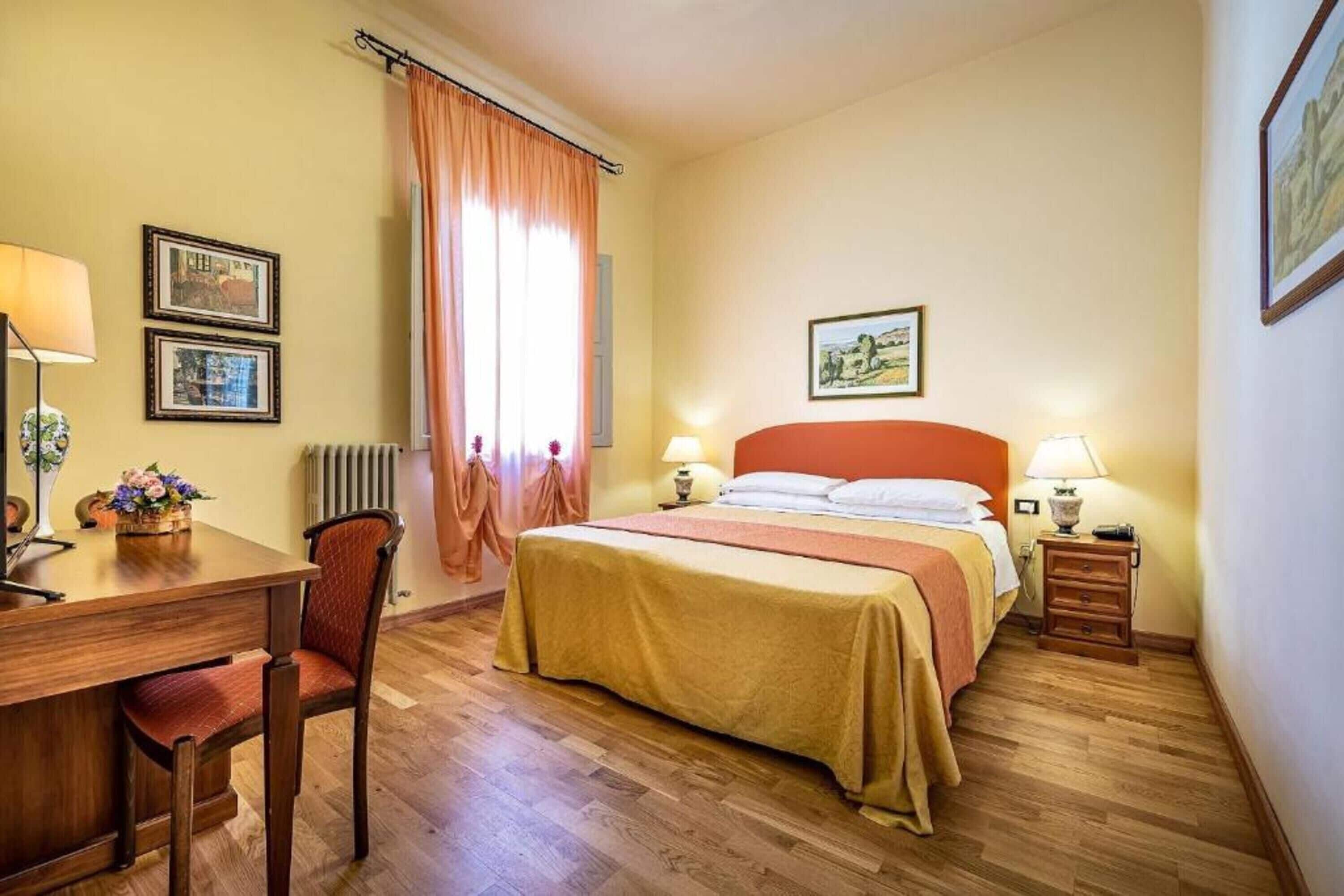 A hotel room with a bed, a desk with a chair, a lamp, and a picture on the wall.
