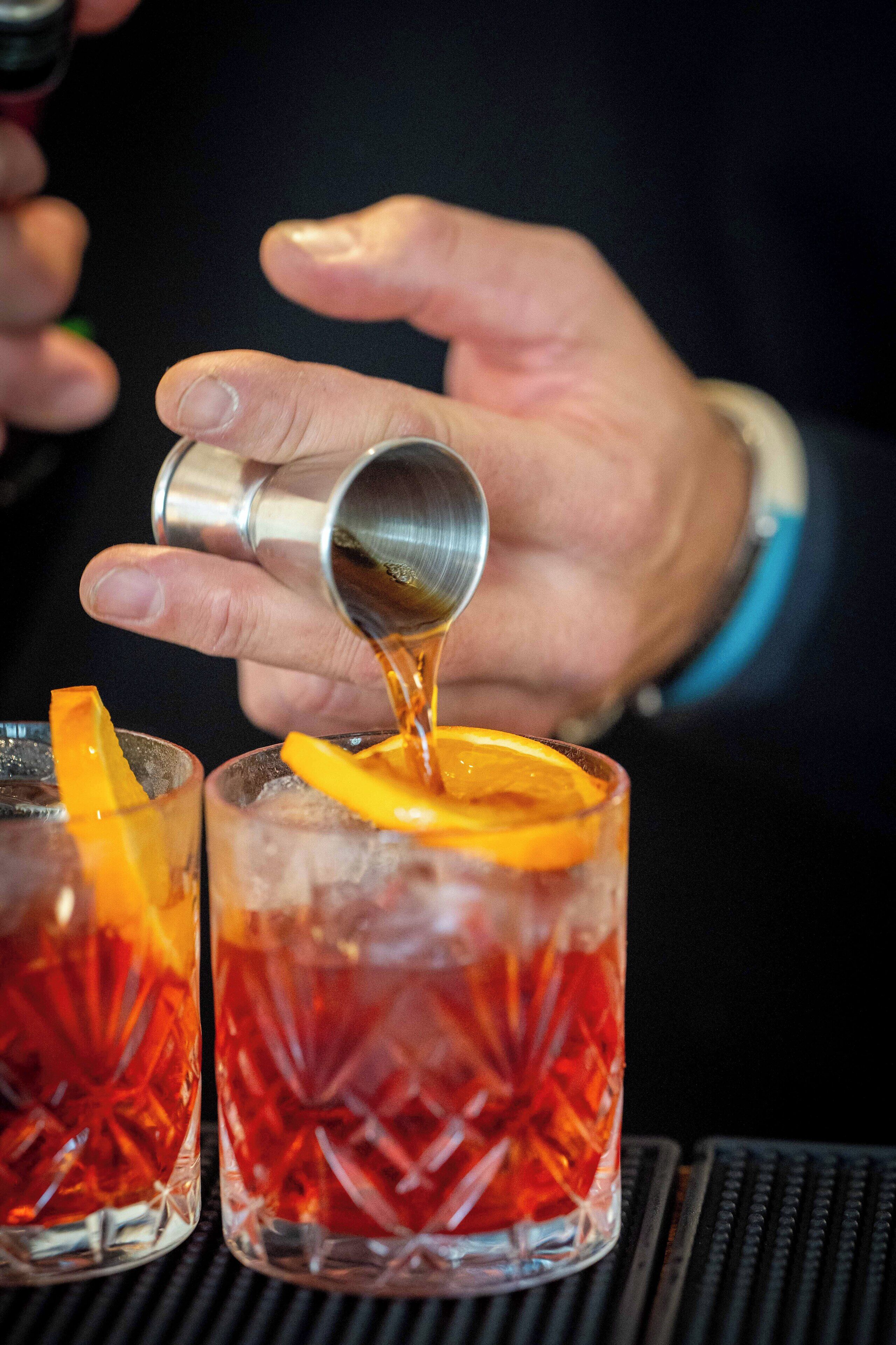 A person pouring a drink into a glass with an orange slice.