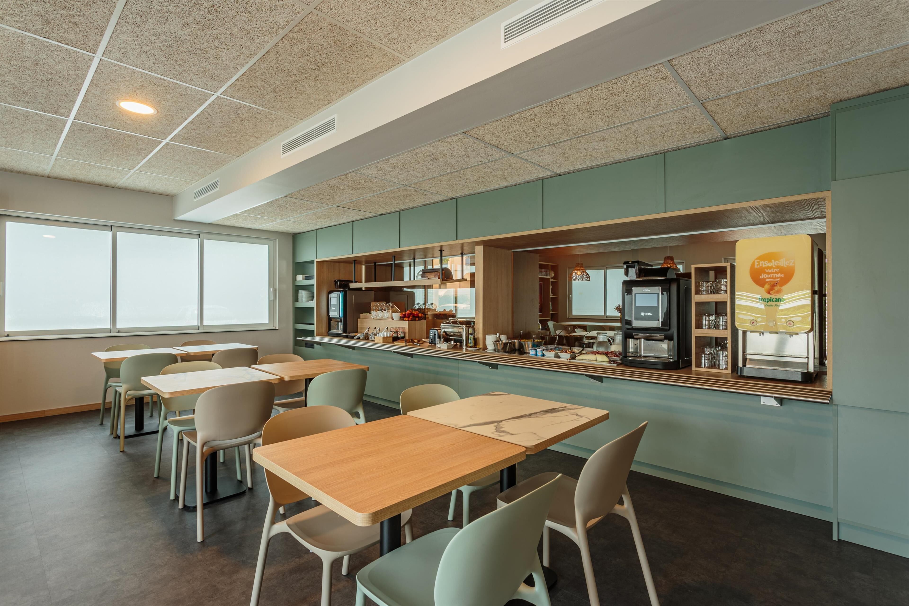 Een modern café met houten tafels en stoelen, een balie met koffieapparatuur, en een groot raam.