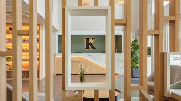 Un moderno vestíbulo de hotel con mostrador de recepción, separadores de madera y suelo de mármol.