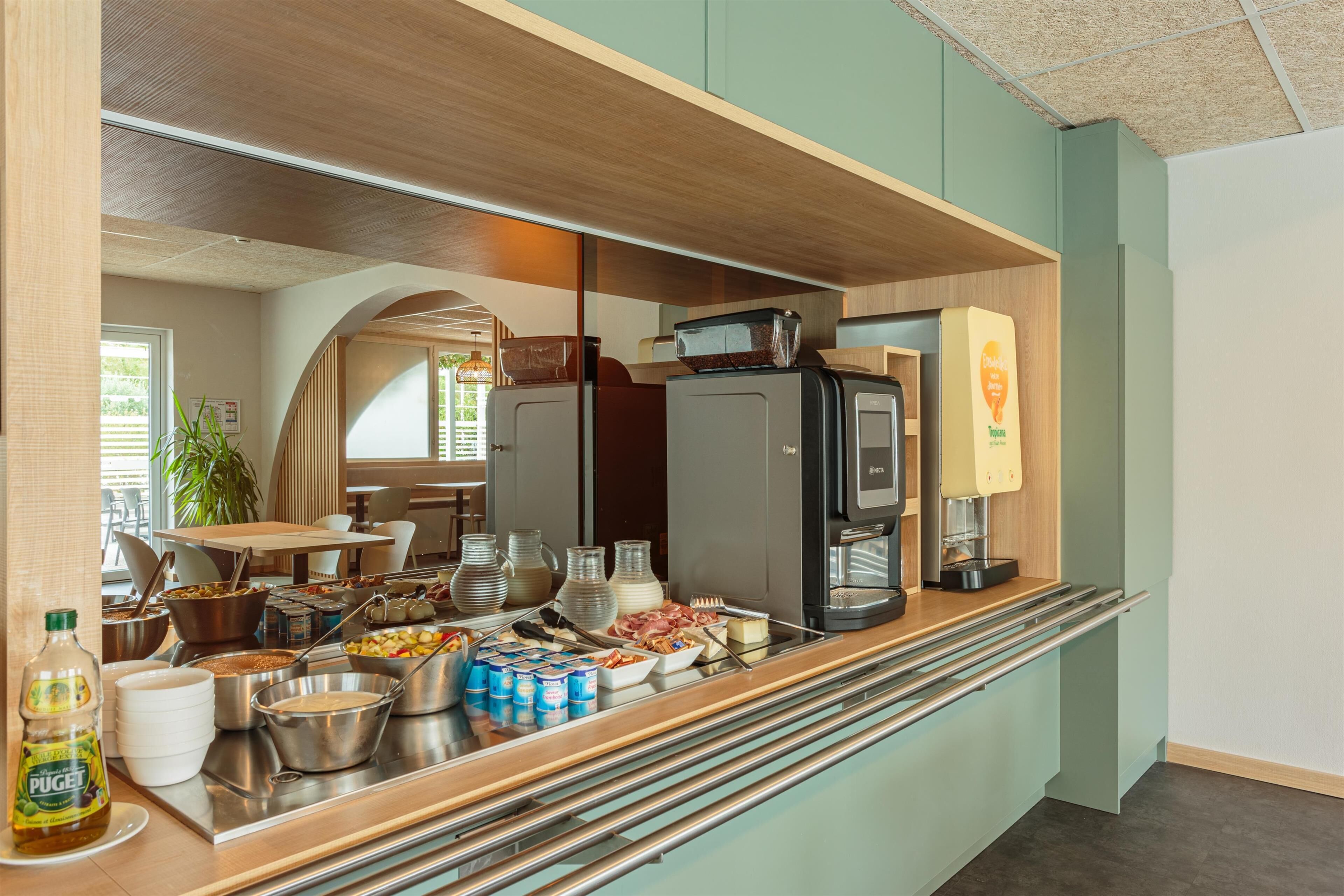 A buffet setup with various food items and beverages, a coffee machine, and a refrigerator.