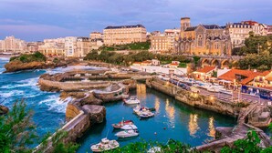 Un pueblo costero con edificios históricos, un puerto con barcos y una iglesia destacada.
